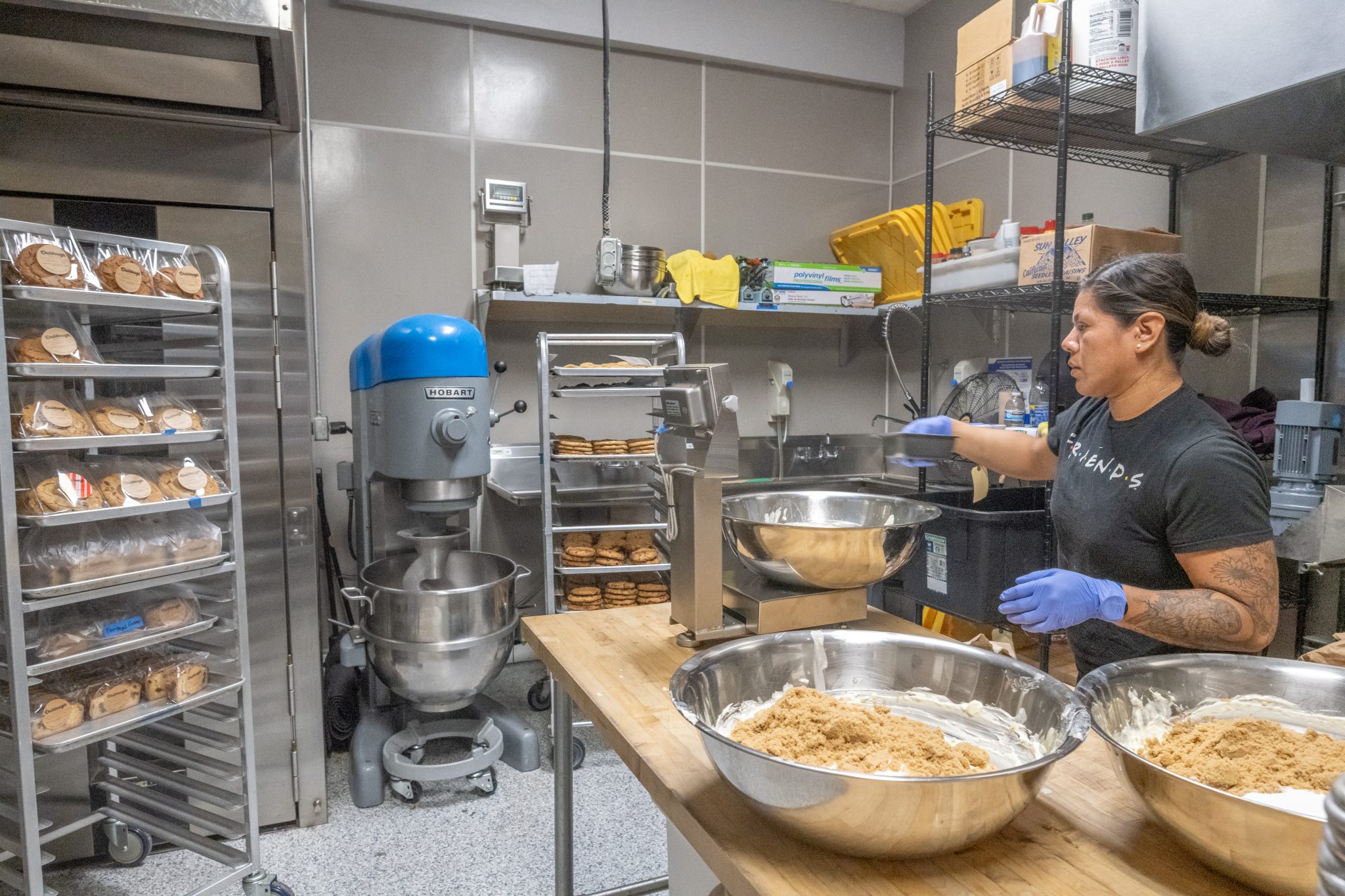 Baker working in a commercial kitchen with mixers and racks of baked goods.