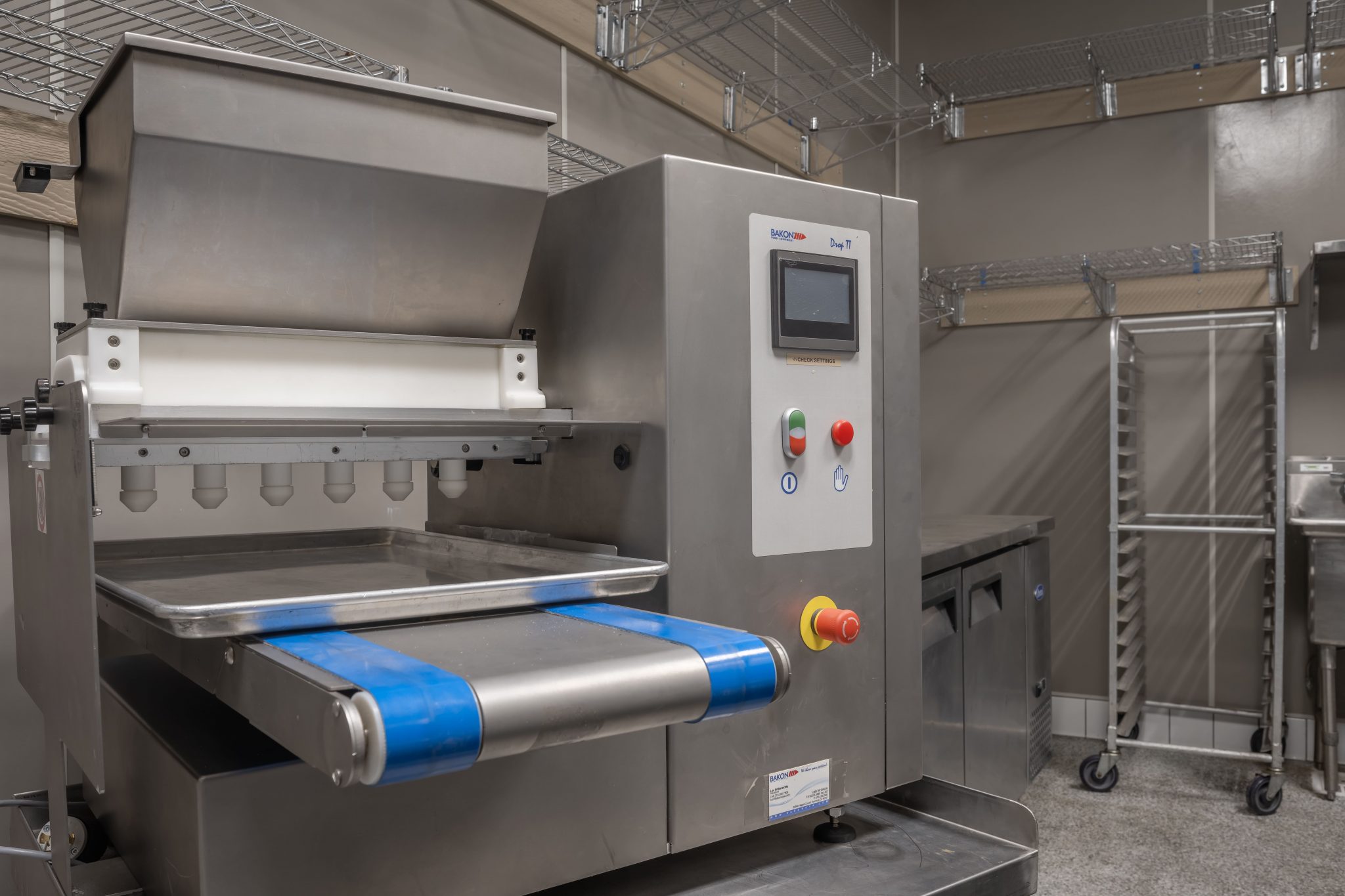 Industrial stainless steel baking machine with a conveyor belt in a kitchen.