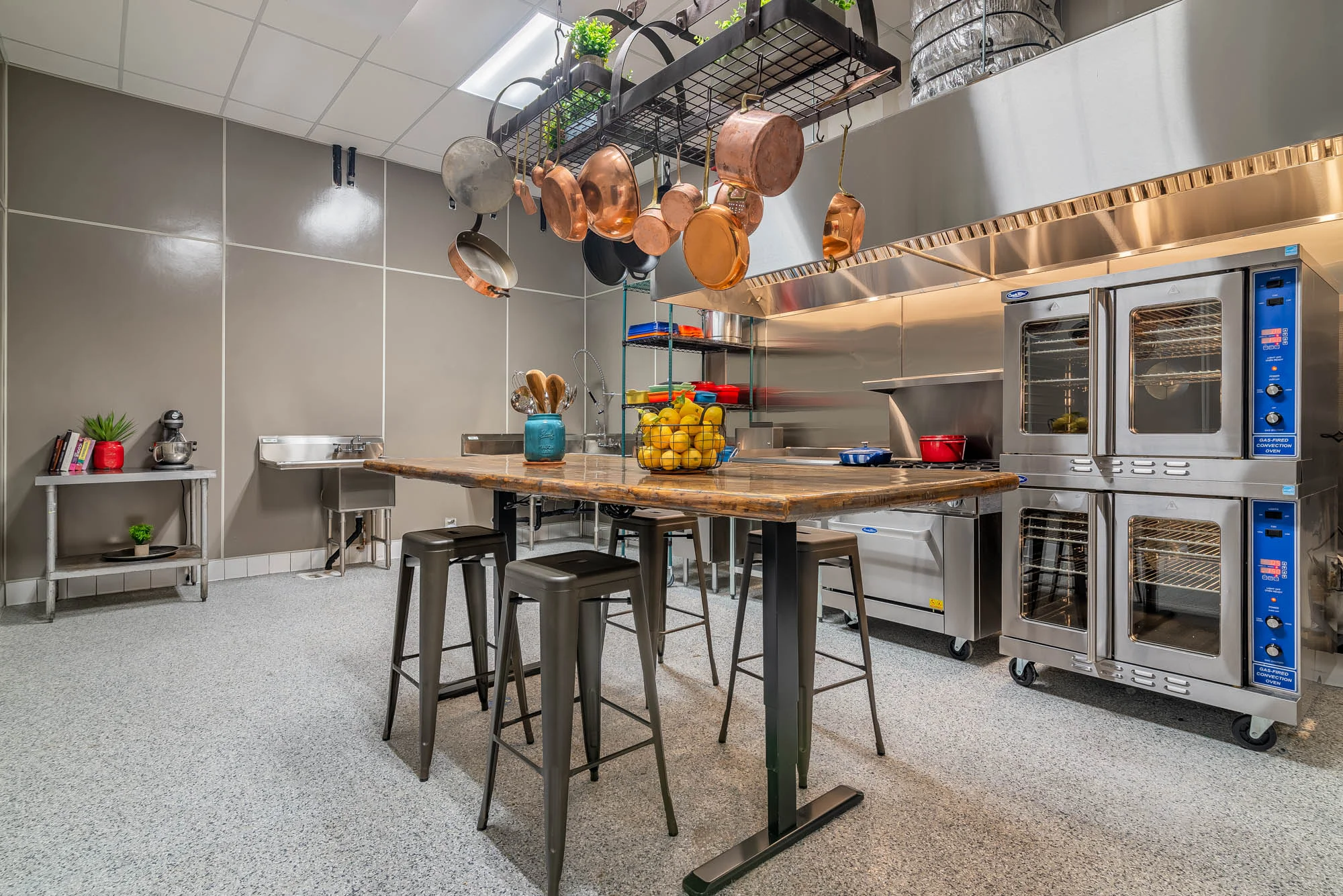 Commercial kitchen with a wooden table, basket of lemons, and cooking equipment.