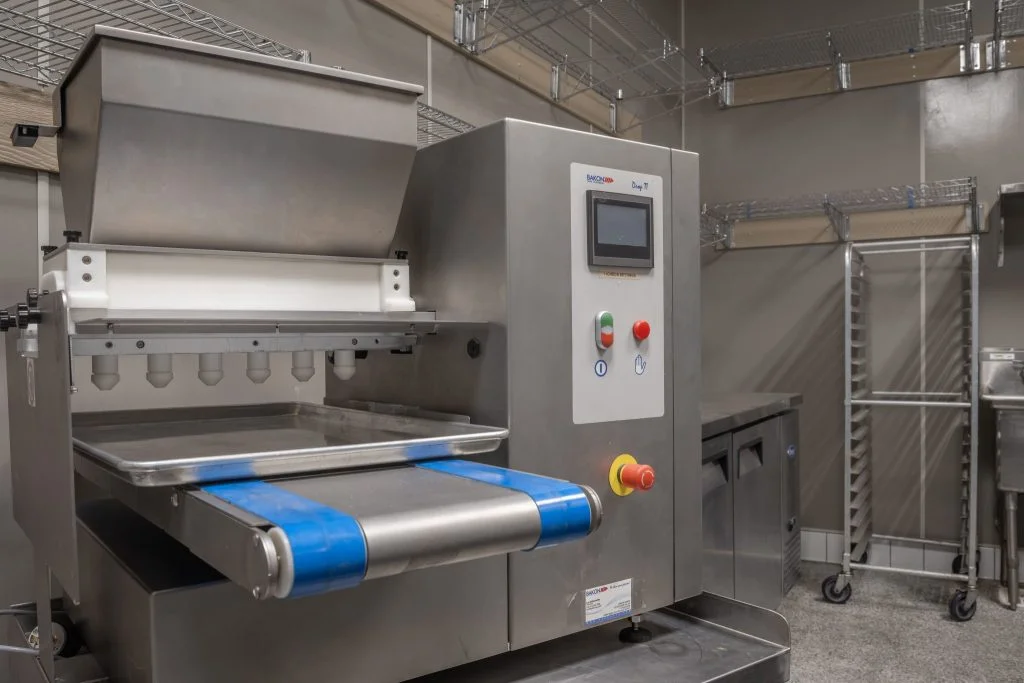 Industrial stainless steel baking machine with a conveyor belt in a kitchen.